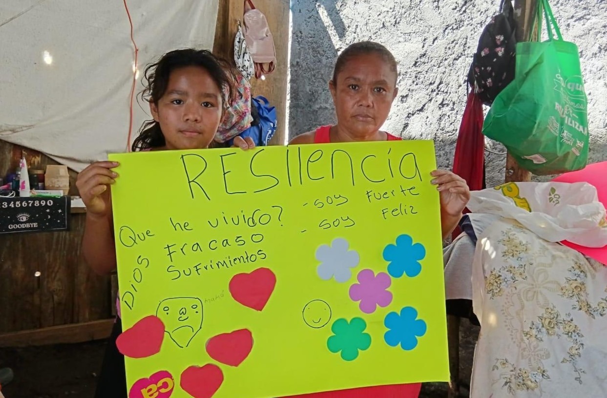 Guatemalan mother and daughter in their home holding a hand-written sign that says "resiliencia", or resiliency.